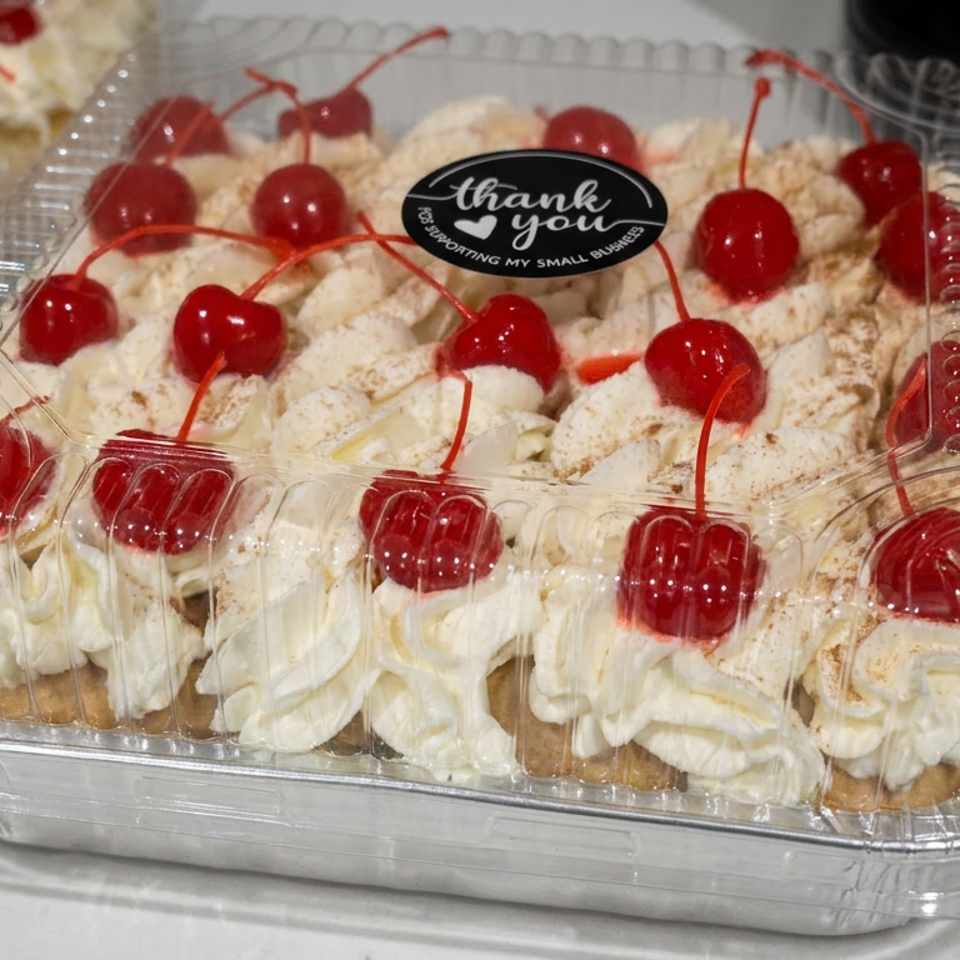 A tray of cream-filled pastries topped with red cherries sits in a clear plastic container.